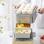 A person in a white shirt is holding a steamer insert loaded with white steamed buns above a multi-compartment steamer basket containing corn and shrimp dumplings, set on a light countertop.
